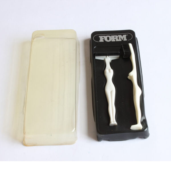Toothbrush and razor blade set shaped like a female body, in white plastic. Cover on the side.