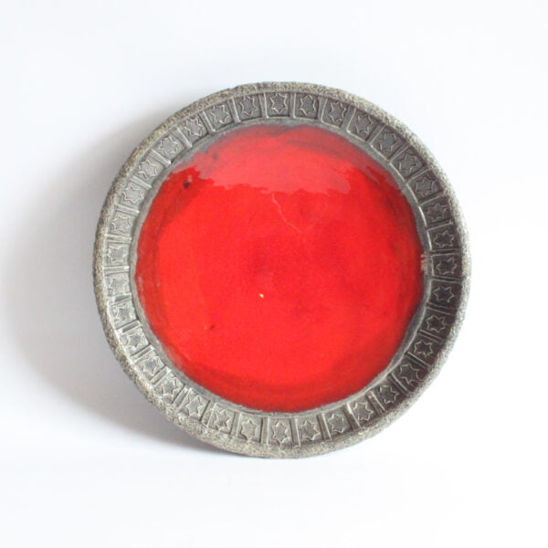 Ceramic bowl with red lava glaze interior, rough dark grey rim imprinted with star shaped symbols. Top view.