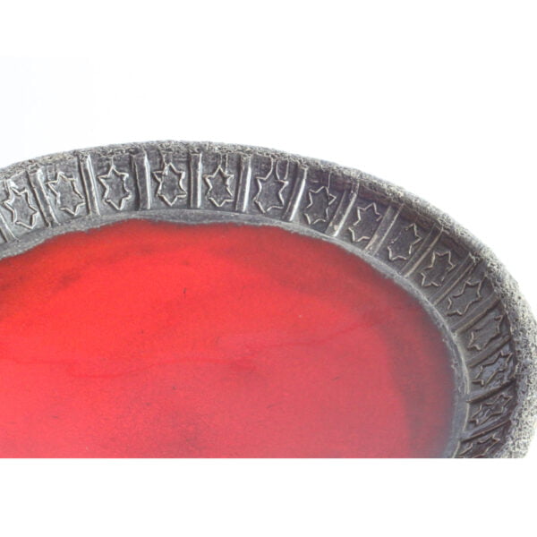 Ceramic bowl with red lava glaze interior, rough dark grey rim imprinted with star shaped symbols. Rim view.