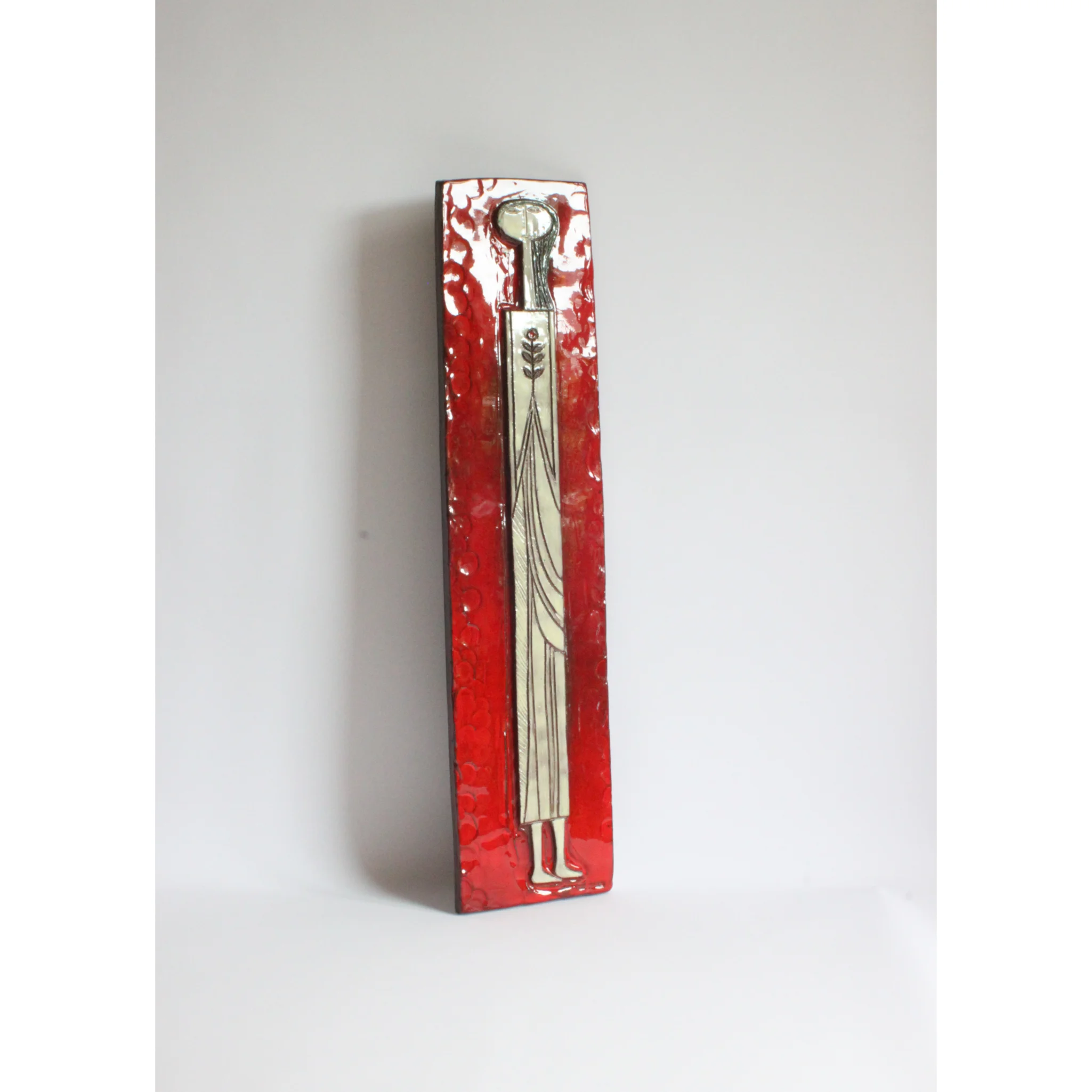 Tall square ceramic wall ornament with a red glaze by Oswald Tieberghien. Depicting a stylized elongated woman in a white dress holding a flower.