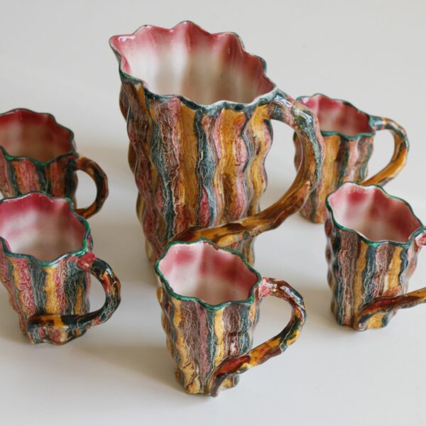 A set of six crazy colorful mugs and a pitchers in Vallauris ceramics, 1960s-1970s. Naturalistic shape where body resembles tree bark, and the handle swings back like a branch. The inside rim resembles a shell.