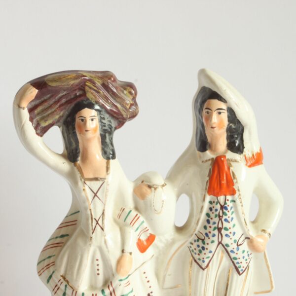 A Staffordshire earthenware figurine sculpture of a Scottish Couple, 19th Century. Both victorian attire, the man wears a hat sidewas and the woman in carrying a bale of clothes? on her head. Decorated with green, blue and brown dots. With red details for the scarf and shoes. Century soup vintage design antiques curiosa collectibles antwerp.