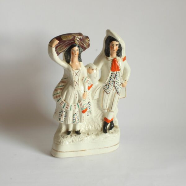 A Staffordshire earthenware figurine sculpture of a Scottish Couple, 19th Century. Both victorian attire, the man wears a hat sidewas and the woman in carrying a bale of clothes? on her head. Decorated with green, blue and brown dots. With red details for the scarf and shoes. Century soup vintage design antiques curiosa collectibles antwerp.