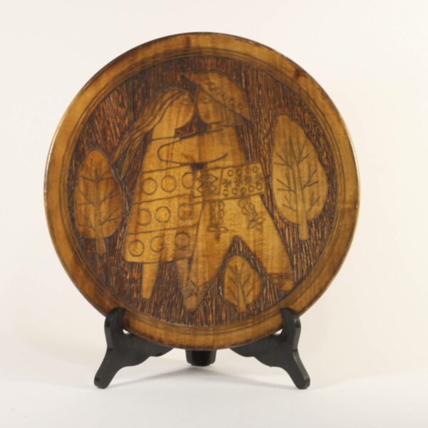 A Scandinavian style carved wooden plate with figures, 1960s - 1970s. Copper inlay outlines the leaves, symbols and figures. Depicting a hippie couple kissing, stylized modernistic. The background seems to be darkened by a hot needle. Dimensions: 28.5cm x 4cm Century soup vintage design antiques curiosa collectibles antwerp.