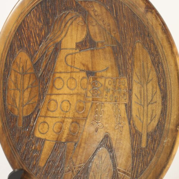 A Scandinavian style carved wooden plate with figures, 1960s - 1970s. Copper inlay outlines the leaves, symbols and figures. Depicting a hippie couple kissing, stylized modernistic. The background seems to be darkened by a hot needle. Dimensions: 28.5cm x 4cm Century soup vintage design antiques curiosa collectibles antwerp.
